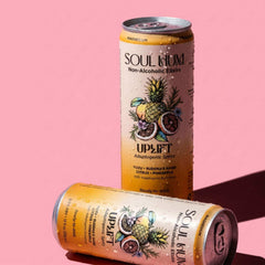 Uplift Adaptogenic Spritz non-alcoholic drink cans in peach and orange, featuring tropical fruit illustrations and pull tabs